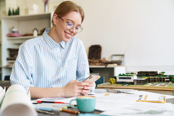 Photo of woman architect using mobile phone while designing draft