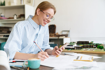 Photo of woman architect using mobile phone while designing draft