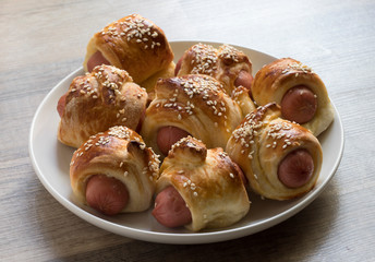 Fresh baked sausages in dough with sesame on a plate.