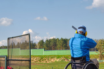 man in a wheelchair shoots clay pigeons, spring blue sky and forest in the background