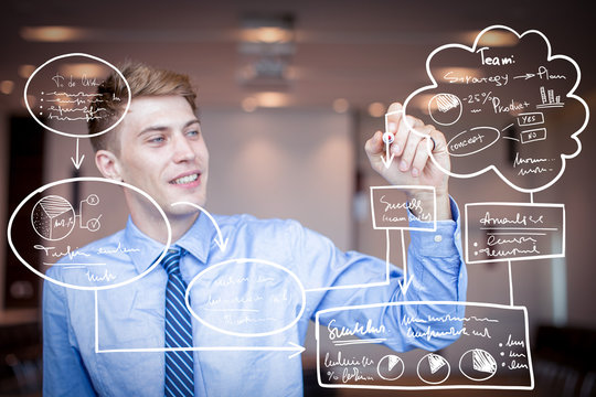 Closeup portrait of smiling adult business man holding marker and drawing virtual management flowchartson transparent board with blurred conference room in background. Front view.