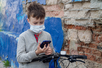 A teenage boy in a mask is standing at the bike and waiting for friends to go for a walk together.