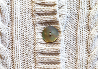 Detail of knitted white cotton with mother of pearl button. Knitting fabric cotton