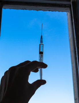 Syringe in hand on bluesky background. Silhouette of syringe in womes hand.