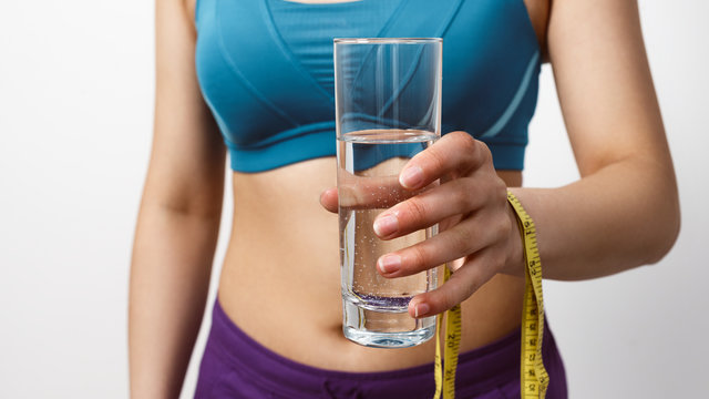 A Slim Woman In Sportswear Holds A Glass Of Water With A Measuring Tape.