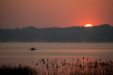 Wędkarze płyną przez jezioro w świerklańcu podczas wschodu słońca.