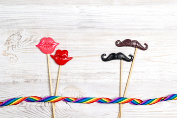 Pair of decorative lips and mustache with rainbow ribbon on wooden background.