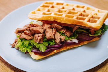 tasty Belgium waffle with lettuce, meat, egg and vegetables served of pretty blue plate