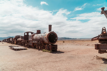 Fototapeta na wymiar Train Cemetry Bolivia Salt Flats. Bolivian salty desert and blue sky background. Shot in Salar de Uyuni. Rusted, waste, abandoned, locomotive graveyard, railroad concepts. Tourist attraction