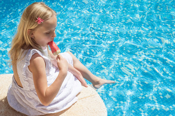 Summertime fun. Happy little girl eating ice cream near the pool