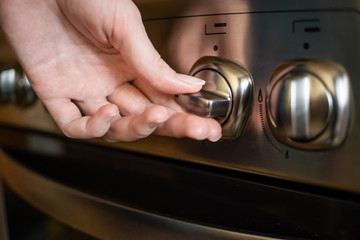 woman's hand turns on a switch on a stainless steel gas stove close up