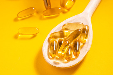 Close-up on a wooden spoon of cod liver oil capsules on orange background