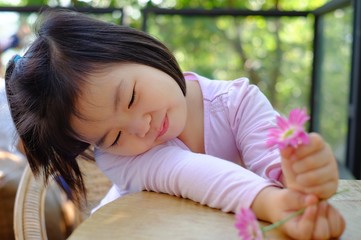 A cute shy Asian girl sitting by a table at a coffee shop, relaxing and enjoy her lovely pink flowers, smiling.
