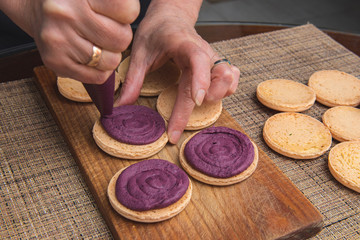 Cooking macarons cookies at home. Female hand squeezes cream on homemade cookie .on a wooden board