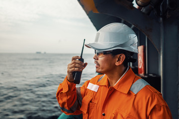 Filipino deck Officer on deck of vessel or ship , wearing PPE personal protective equipment. He speaks to VHF walkie-talkie radio in hands. Dream work at sea