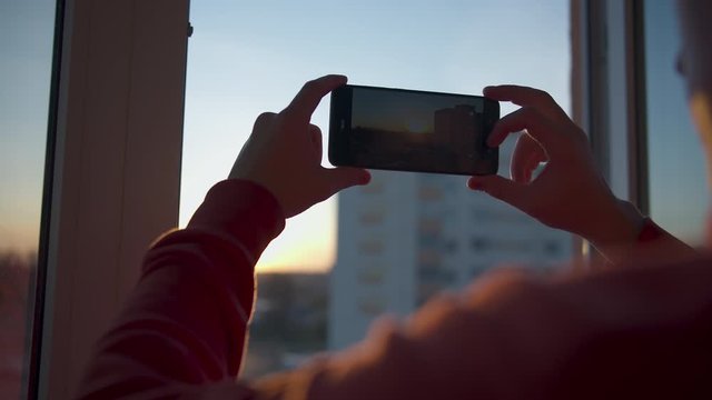 Man holds a mobile phone and takes off the sunset