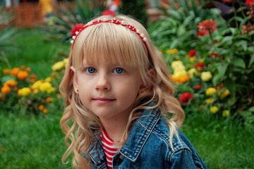 Cute little girl with curly blond hair in a park on a summer day. Close-up portrait of a blue-eyed girl.