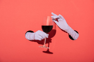 cropped view of woman in gloves holding glass with red wine on red