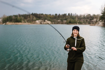 Fisherman with rod, spinning reel on the river bank. Fishing for pike, perch, carp. Woman catching a fish, pulling rod while fishing at the weekend. Girl fishing on lake, pond with text space.