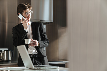 Photo of young businessman talking on cellphone while drinking coffee