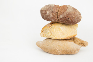 Fototapeta na wymiar Pile of three wheat and rye breads on left side. Fresh crusty baked loafs and pastry isolated on white background. Studio shot. Side view. Homemade food and baking at home concept