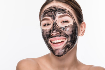 Young girl with a black cosmetic mask on her face holding a brush isolated on a white background