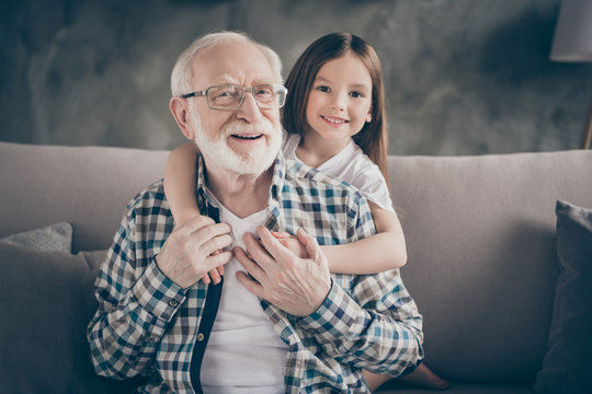 Photo Of Funny Two People Old Grandpa Little Granddaughter Sitting Sofa Stay House Quarantine Safety Hugging Piggyback Modern Design Interior Living Room Indoors