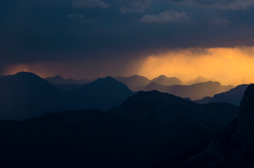 rain clouds at sunset with dark silhouette of mountains
