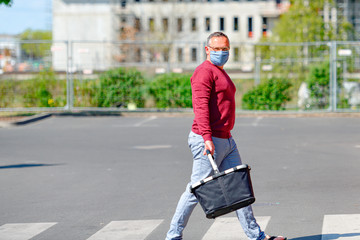 Mann mit Mund-Nasenschutz wegen der Corona-Krise auf dem Weg zum Supermarkt mit Einkaufskorb