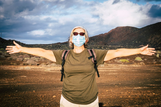 Senior woman with medical face mask enjoys nature outdoors in the mountains. Partial conquest of freedom after coronavirus lockdown