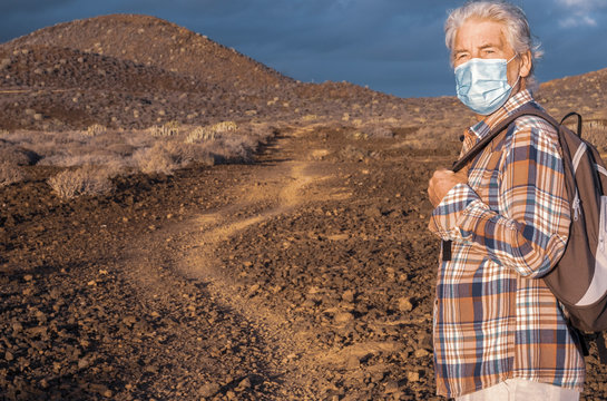 Senior man with medical face mask walks in mountain footpath in arid landscape. Partial conquest of freedom after coronavirus lockdown