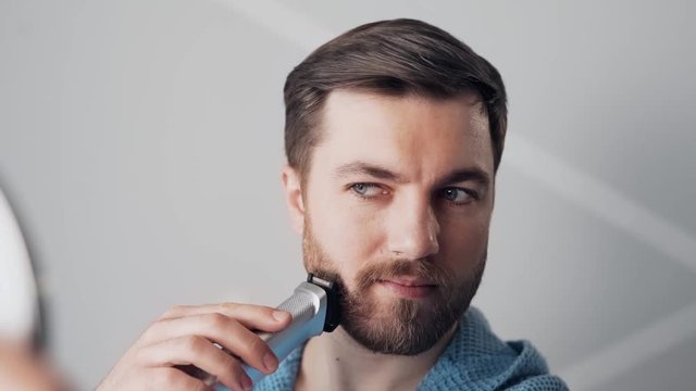 handsome bearded man shaves his beard with a clipper