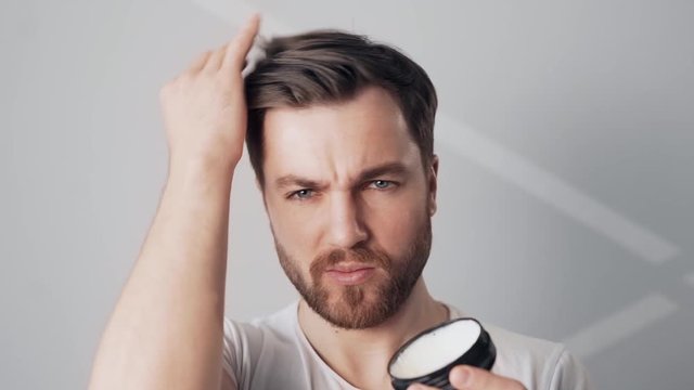 handsome bearded man styles his hair with wax