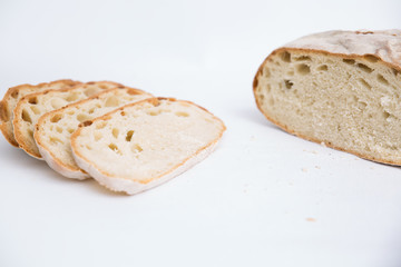 Cut freshly baked loaf of wheat bread and slices. Closeup shot. Isolated object on white background. Homemade food or breakfast concept