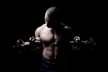 Fototapeta na wymiar Attraktiver und muskulöser Mann posiert mit Hanteln vor schwarzem Hintergrund 