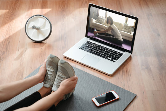 Flexibility and strength. Fit young woman stretching muscles at home, doing exercises while watching yoga tutorial online on laptop. Fitness and home yoga concept