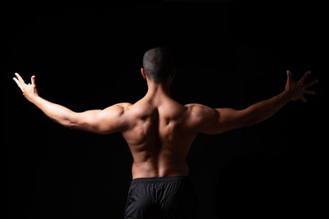 Fototapeta na wymiar Ein Mann mit muskulösem Rücken vor schwarzem Hintergrund, angespannte Rückenmuskulatur 