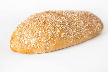 Wheat bread with cereal grains laying at table. Fresh loaf isolated on white background. Selective focus. Side view. Homemade bakery and cooking at home concept