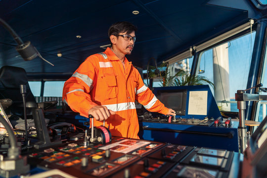 Filipino deck Officer on bridge of vessel or ship wearing coverall during navigaton watch at sea . He is maneuvering with cpp thrusters propulsion