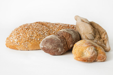 Delicious crunchy white and brown breads. Pastry, loafs and buns laying together and isolated on white background. Studio shot. Side view. Homemade bakery and cooking at home concept