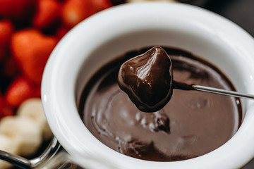 Dipping fresh strawberry into pot with tasty chocolate fondue, closeup shot. Chocolate glaze.