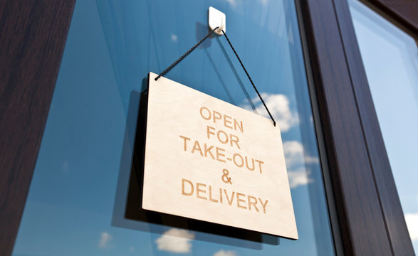 The wooden sign with text: Open for take-out and delivery hanging on the door in cafe