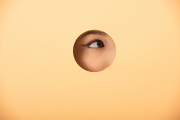 cropped view of woman looking away through hole on pastel orange