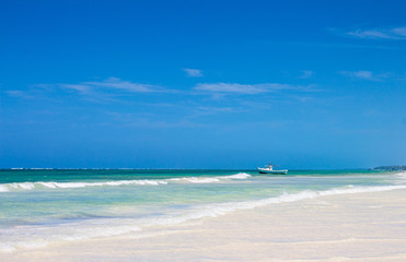 White sand beach, blue sky and white boat