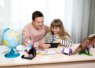 Two children at a desk with a tablet learn at home on the Internet. Home education, distance learning during CoVid-19 quarantine