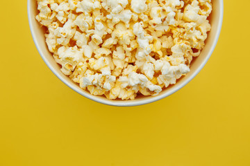 Popcorn in a bowl on yellow background, top view. Entetainement concept.
