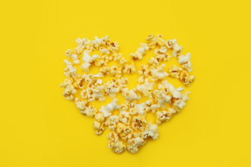 Love Cinema concept of popcorn arranged in a heart shape on yellow background.