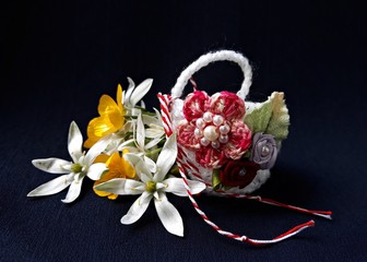 Handmade crocheted basket with spring flowers and red and white string, known as Martisor, it is a...