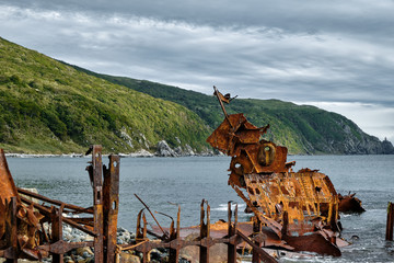 Abandoned old rusty boat on the sea shore with beautiful sky and green hills background. Nature...
