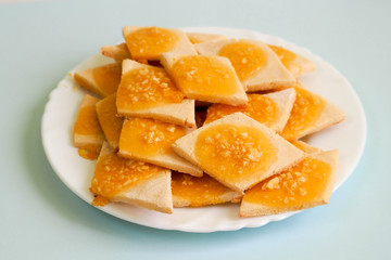 rhombus-shaped rice flour and cottage cheese cookies with orange jam and crushed almonds on a round pink plate on a blue background. gluten-free diet. homemade cookies. nut sprinkles